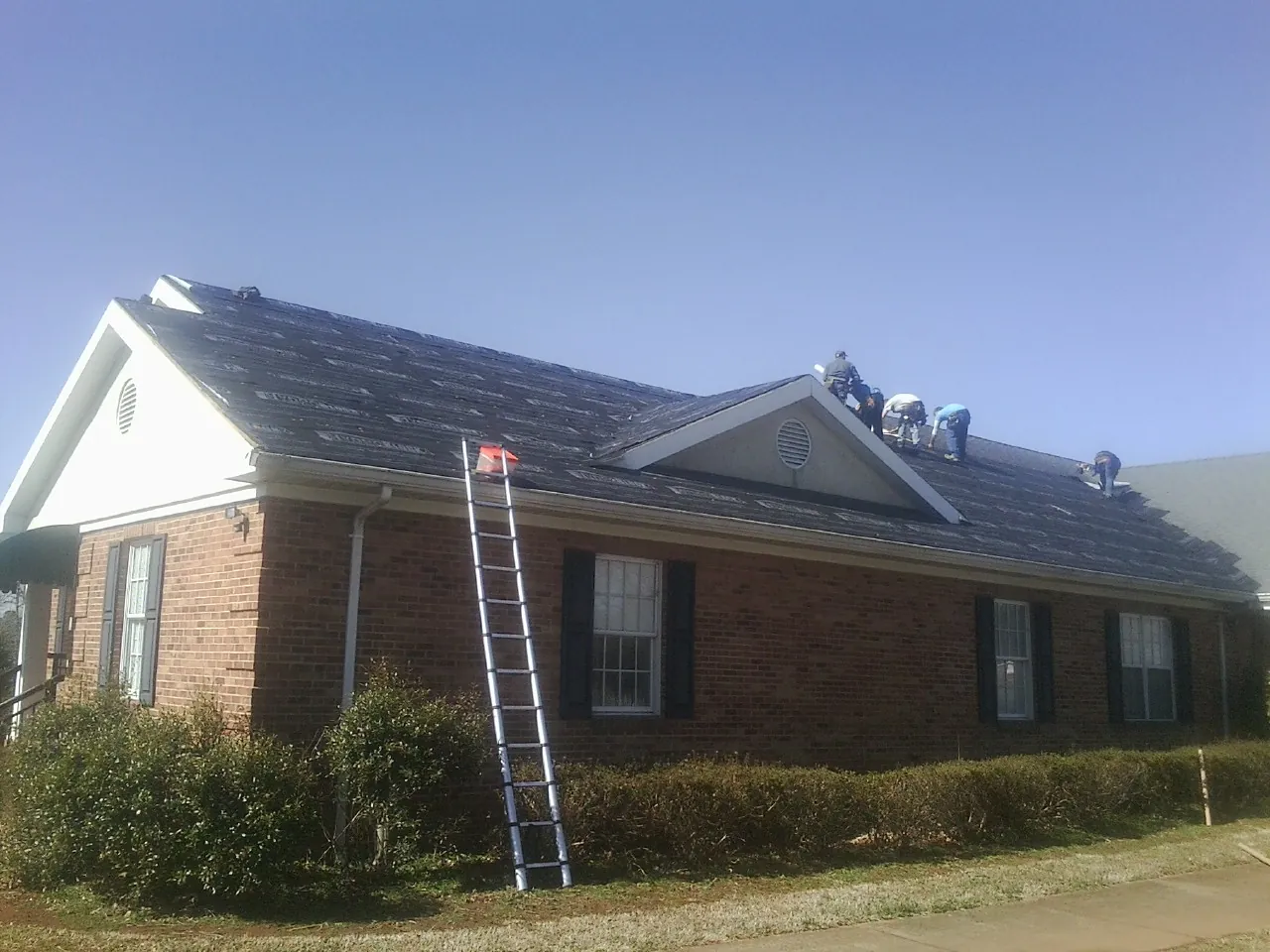 Crew tearing shingles off a brick ranch roof with a ladder set — Metal Roof Repair work by our crew in Cream Ridge