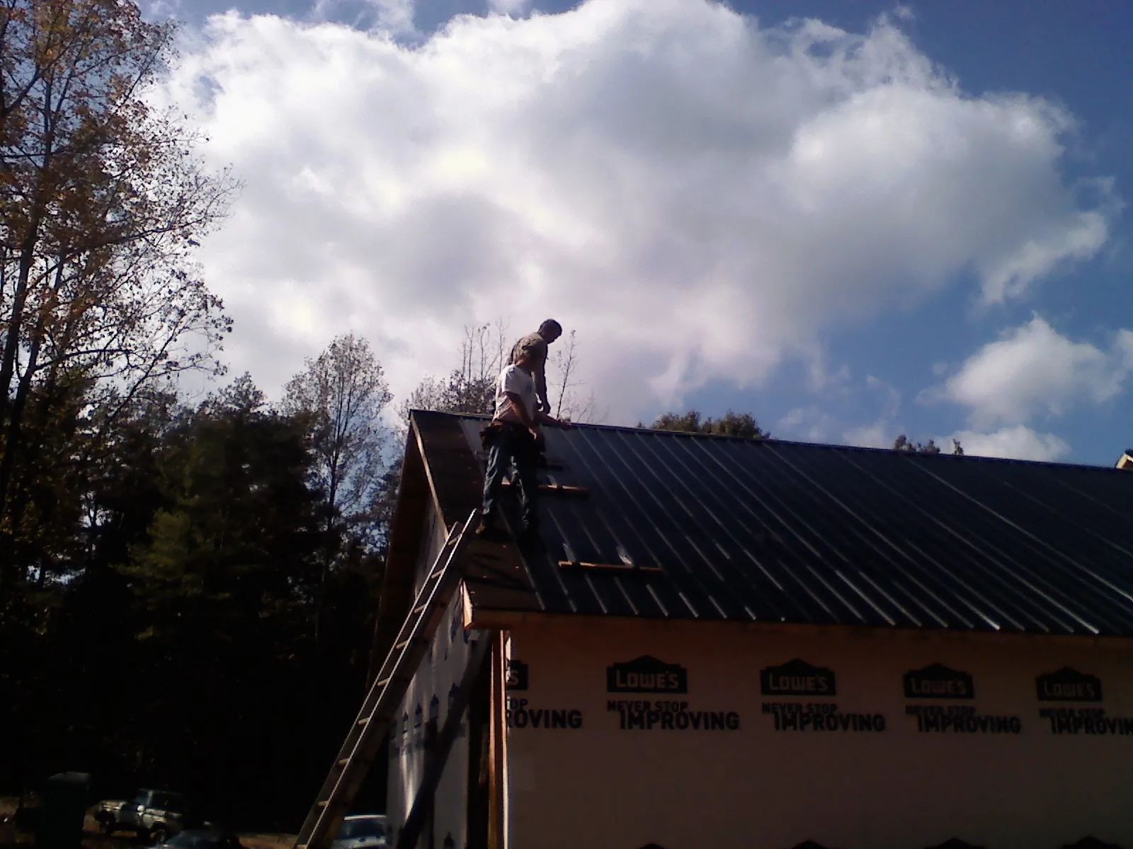 Roofer fastening dark metal panels high against a cloudy sky, from a Roof Inspection job in Cream Ridge