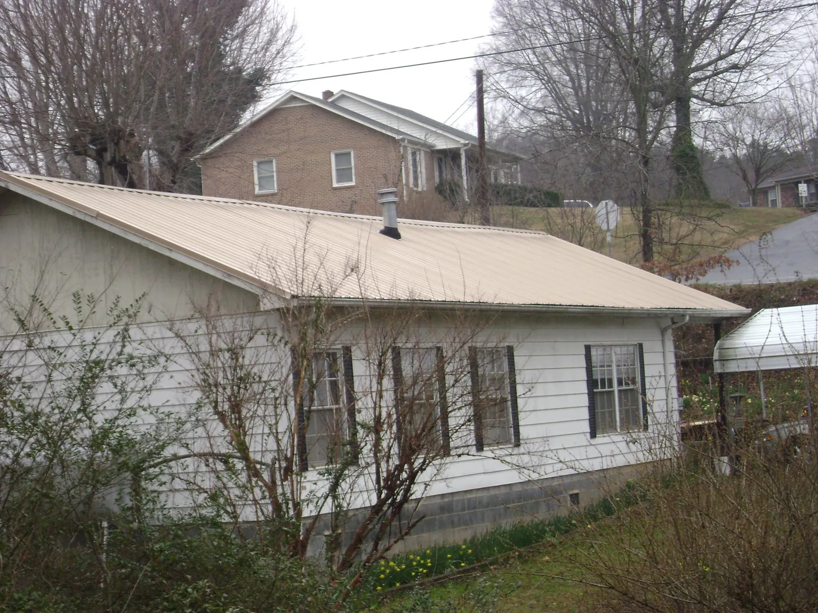 Tan metal roof on a white sided house set into a hillside — Commercial Roofing by Roofing Brothers in Cream Ridge